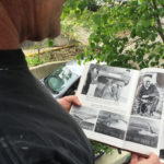 David Christensen on the porch of Seattle Rainiers broadcaster Leo Lassen’s old house in Wallingford looking at a photo of Lassen in front of the same house five decades ago.