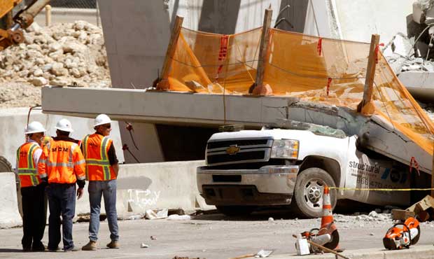Workers stand next to a section of a collapsed pedestrian bridge, March 16 near Florida Internation...