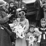In this March 30, 1942 file photo, Cpl. George Bushy, left, a member of the military guard which supervised the departure of 237 Japanese people for California, holds the youngest child of Shigeho Kitamoto, center, as she and her children are evacuated from Bainbridge Island, Wash. Roughly 120,000 Japanese immigrants and Japanese-Americans were sent to desolate camps that dotted the West because the government claimed they might plot against the U.S. (AP Photo/File)
