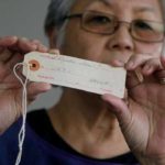 In this Feb. 10, 2017 photo, Satsuki Ina holds up an identification tag issued to her mother, Shizuko Ina, at her home in Oakland, Calif. As Japanese Americans mark the 75th anniversary of the executive order that authorized their incarceration, they're speaking out against new presidential orders that limit travel and target immigrants. (AP Photo/Jeff Chiu)