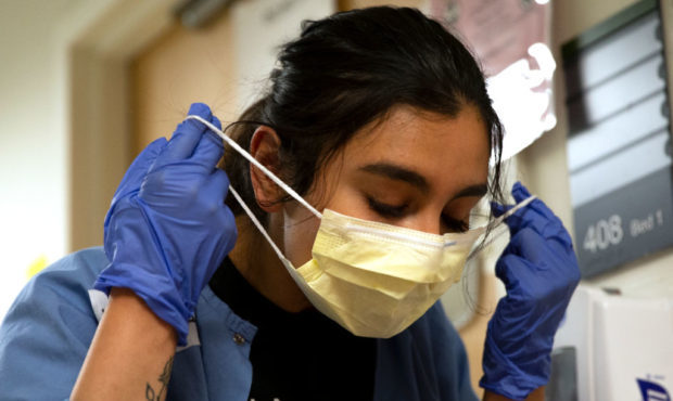 Charge nurse Liliana Palacios carefully removes her mask and PPE after tending to a patient with CO...