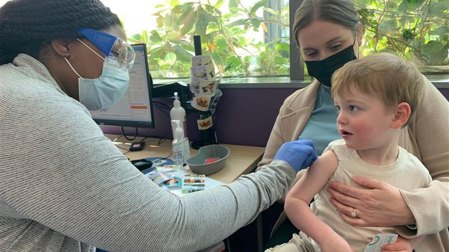 Cade Simeona receiving his first dose of the COVID-19 vaccine, held by his mother Cassie Simeona...