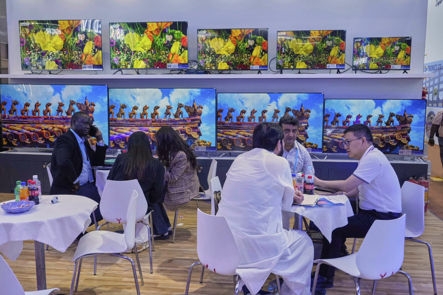 FILE - Visitors talk to a sale rep for televisions at the 137th Canton Fair, in Guangzhou in southe...