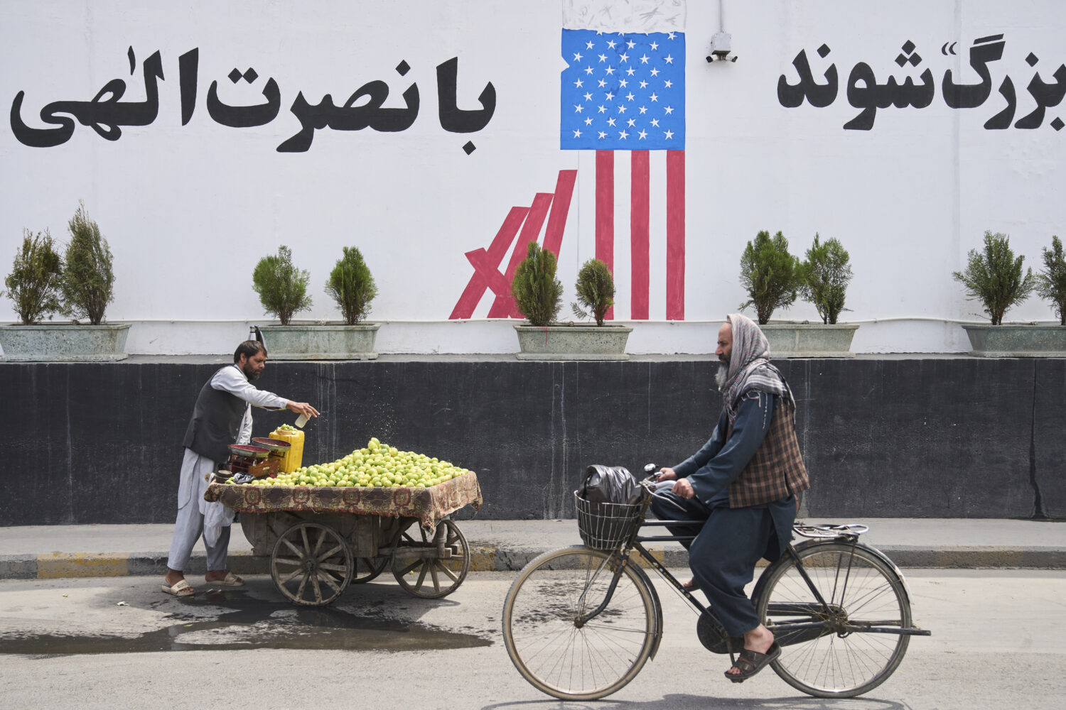 A cyclist passes in front of the former US embassy while a vendor waits for customers, in Kabul, Af...