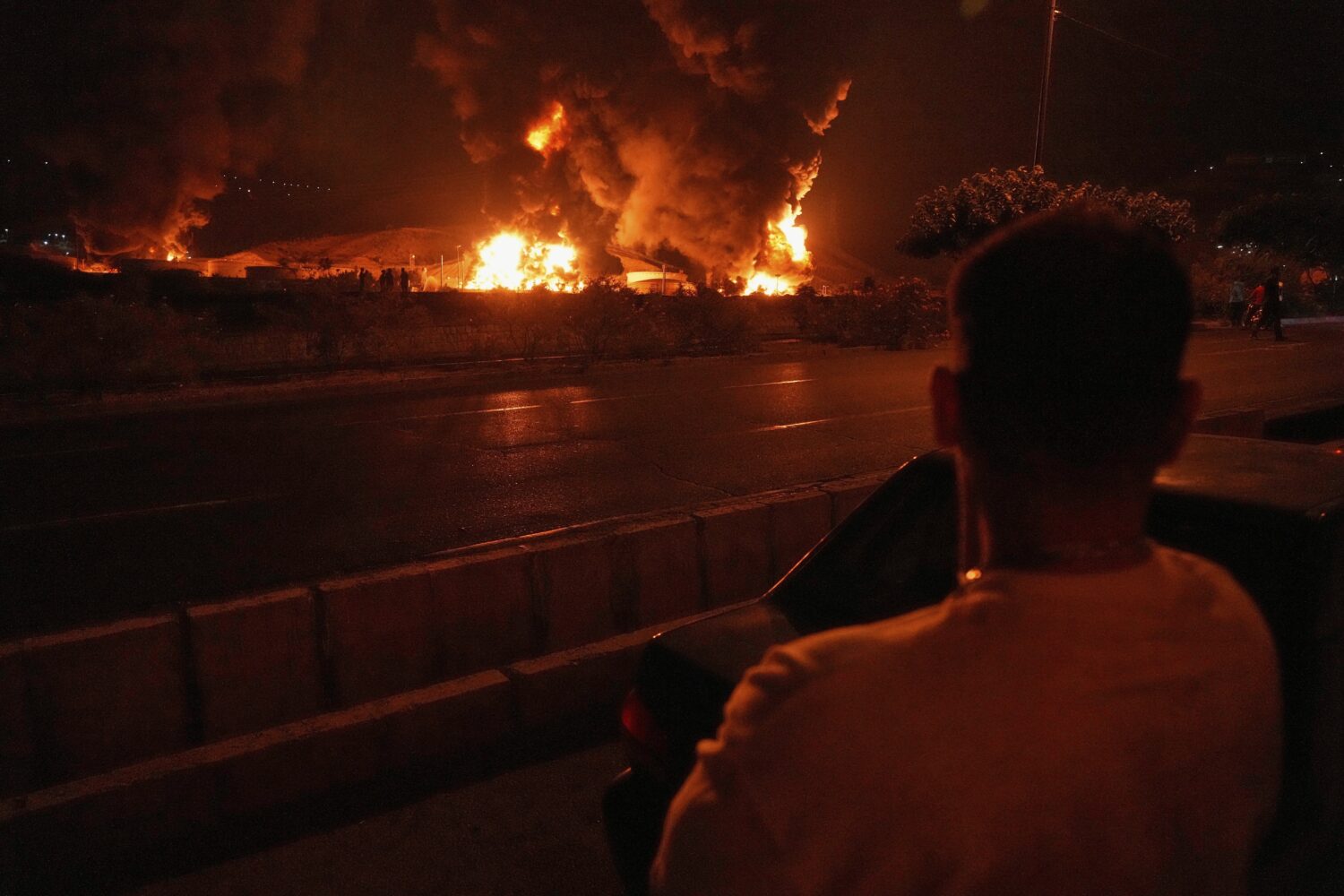 A man looks at flames rising from an oil storage facility after it appeared to have been struck by ...