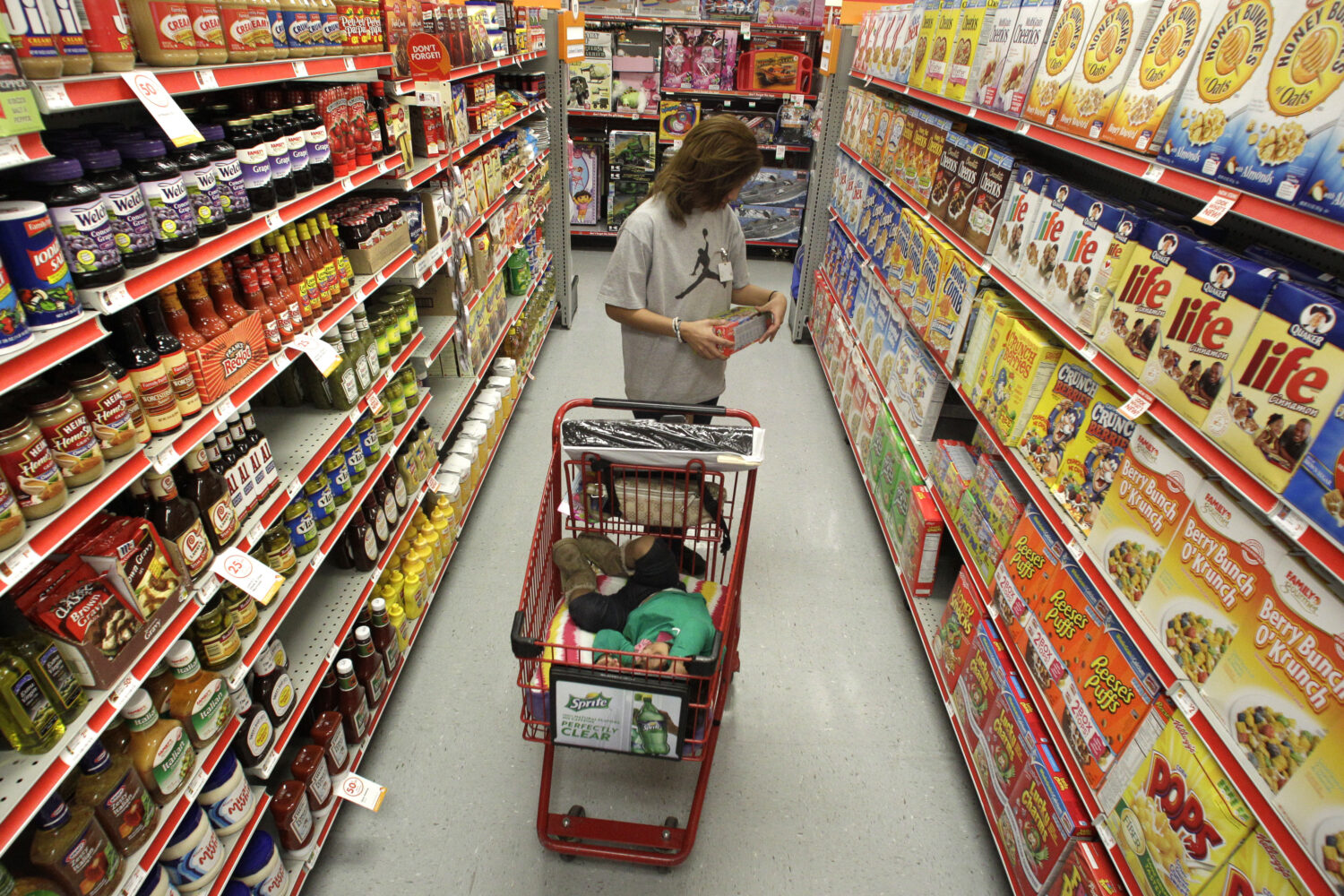 FILE - A woman looks at products in the aisle of a store as her daughter naps in the shopping cart ...