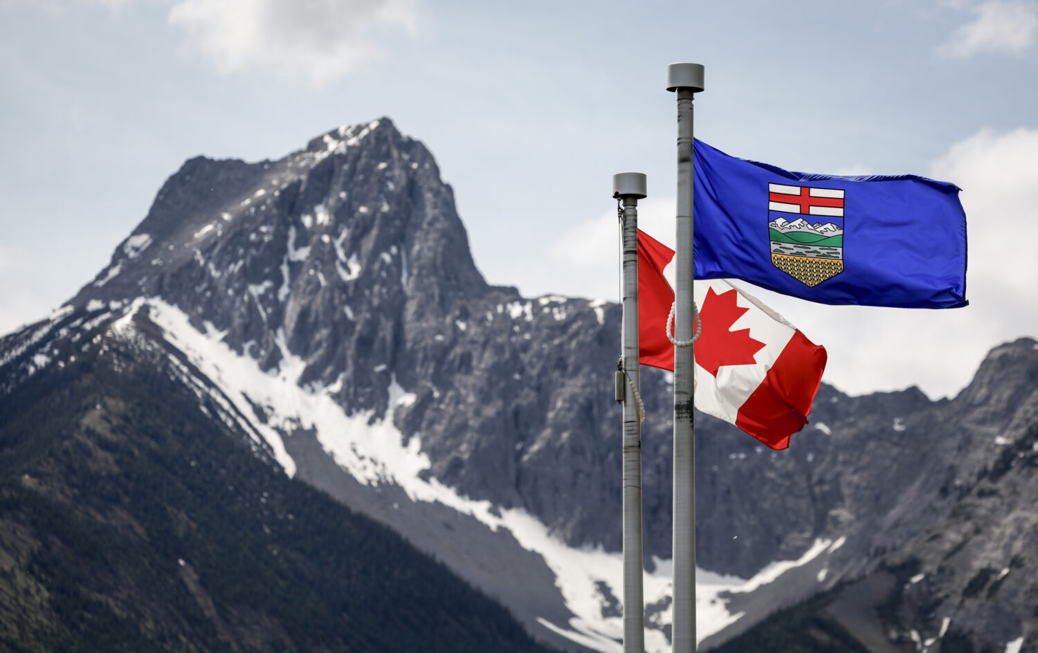 FILE - A Canada flag, left, and an Alberta flag flap in the breeze with Wedge Mountain in the backg...