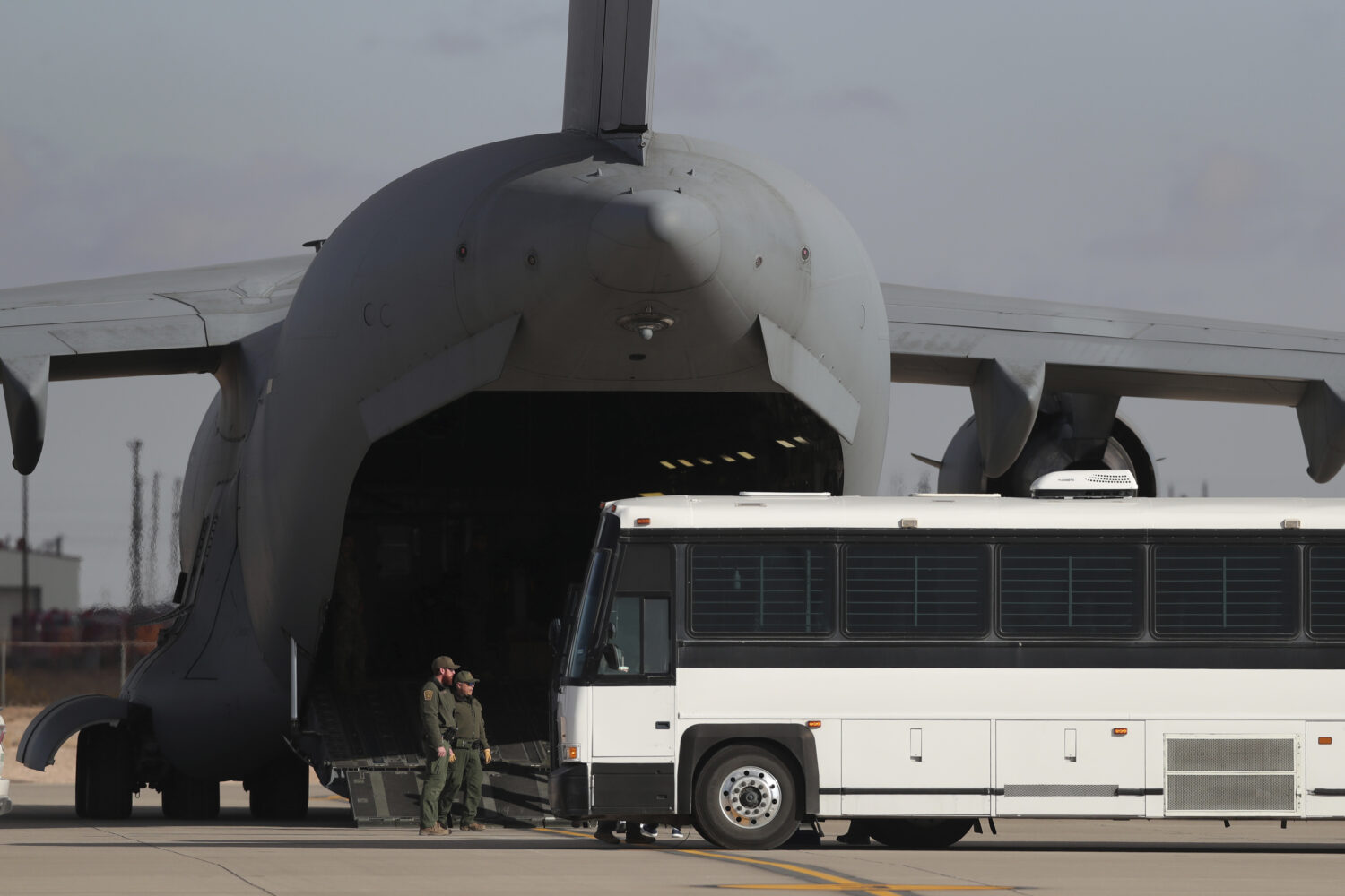 FILE - A military aircraft waits for migrants to board from a bus at Fort Bliss in El Paso, Tx., Th...