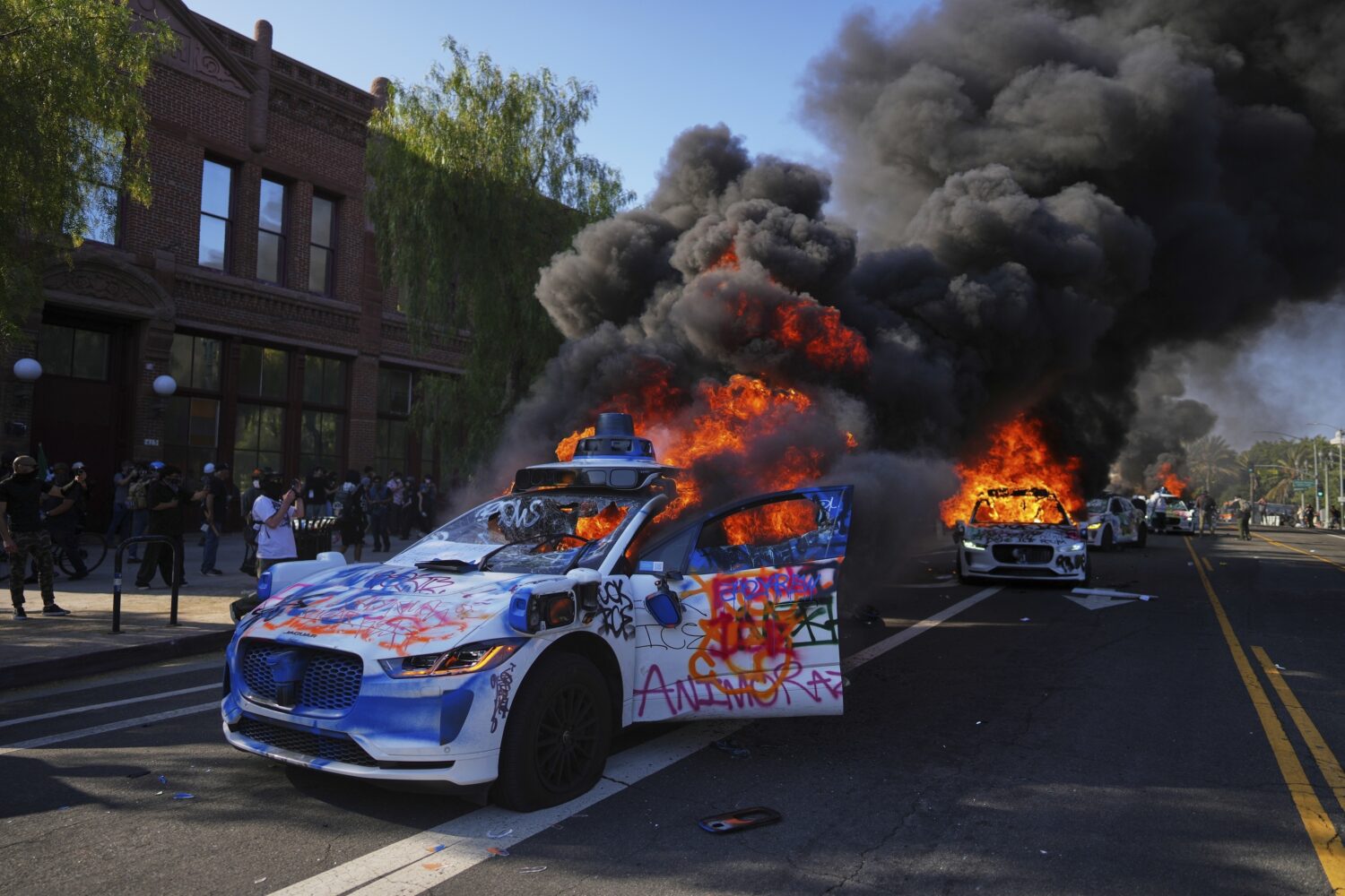 FILE - Multiple Waymo taxis burn near the Metropolitan Detention Center of downtown Los Angeles, Su...