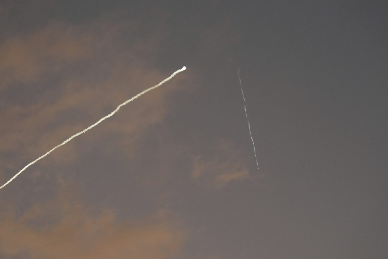 A smoke trail from the Israeli Iron Dome air defense system streaks across the sky as it intercepts...