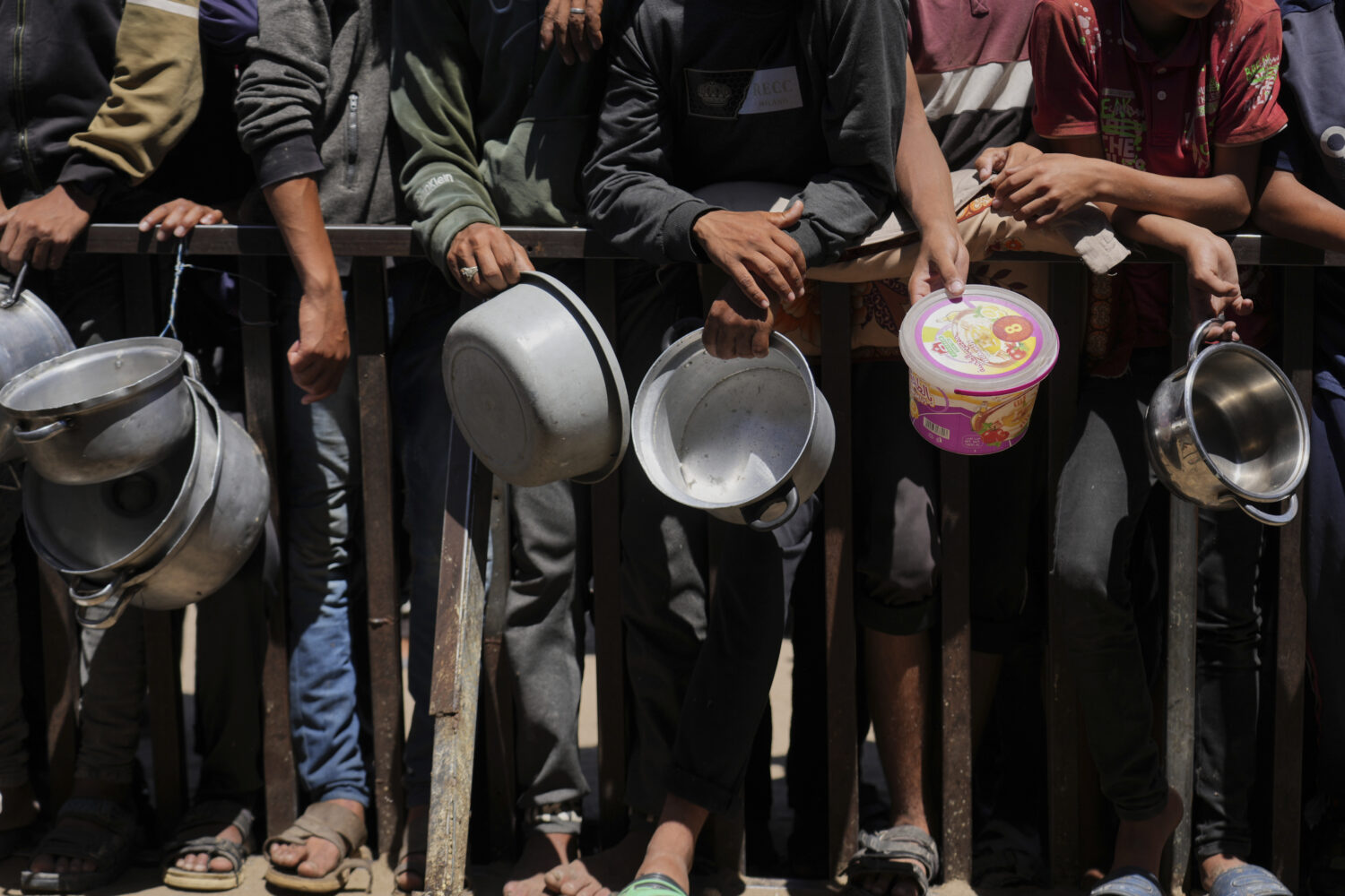 Holding their pots, Palestinians wait to get donated food at a community kitchen in Khan Younis, so...