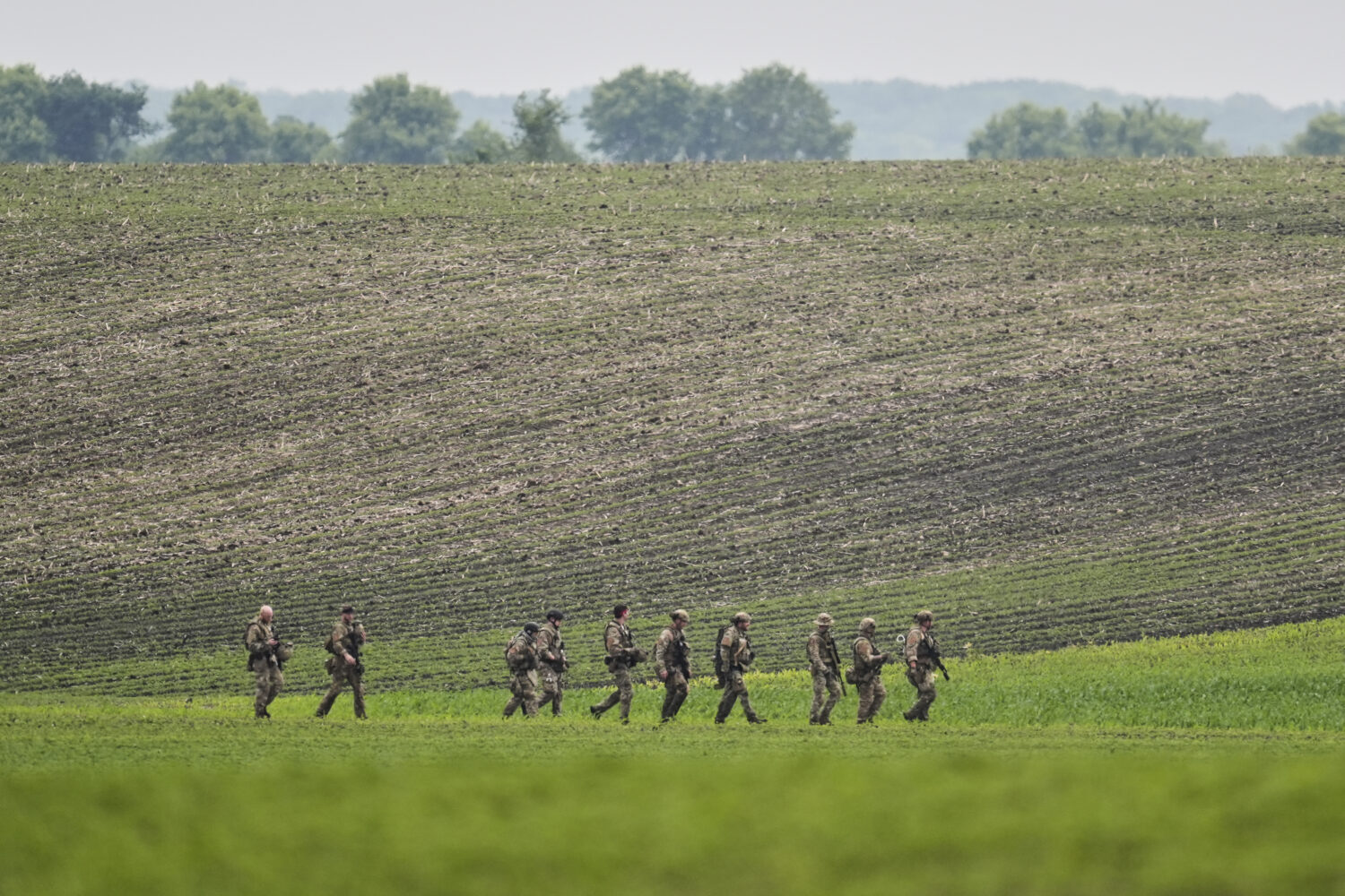 Members of law enforcement agencies walk through a field near a vehicle suspected to belong to shoo...