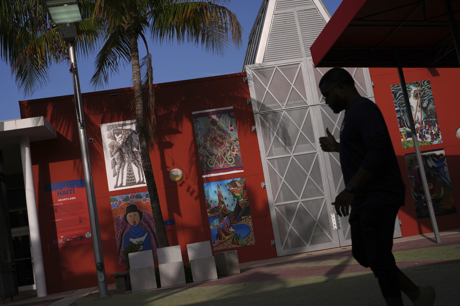Haitian art is displayed on a wall as a man practices dance moves for a father-daughter performance...