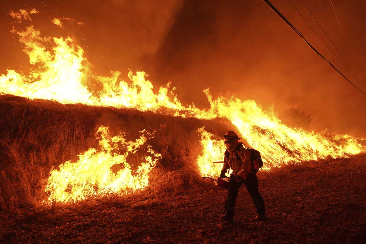 A firefighter carries a drip torch as he ignites a backfire against the Hughes Fire burning along a...