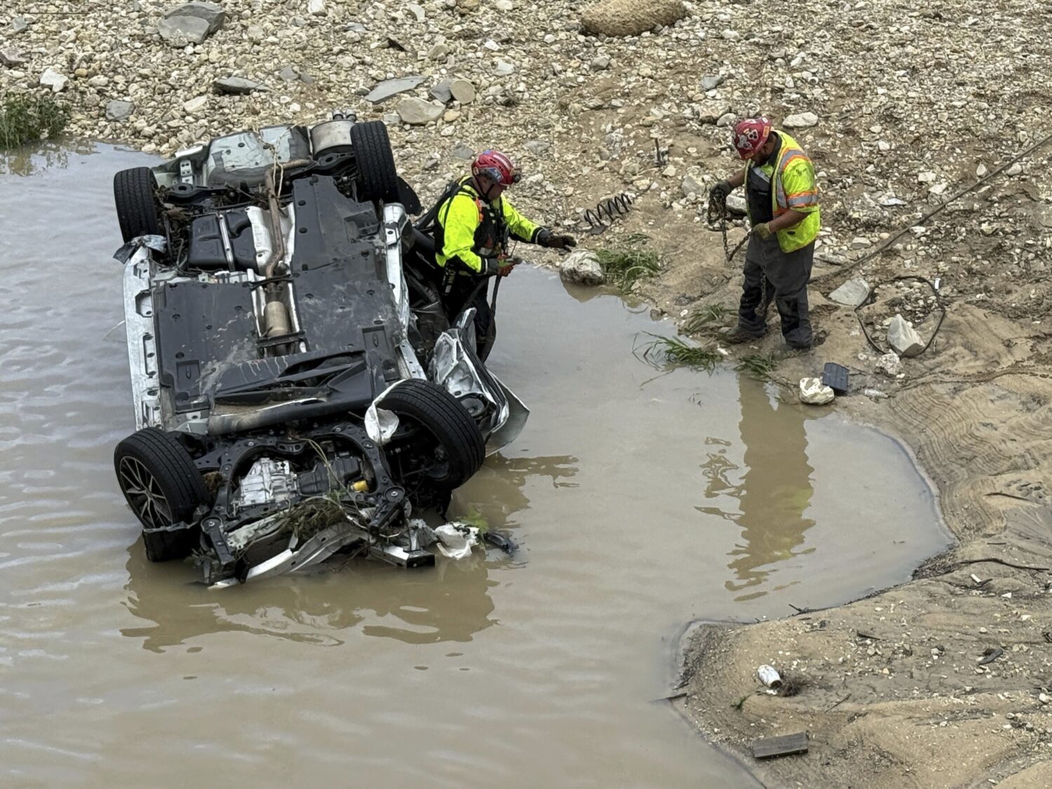 A crew works near a vehicle that was swept away in floodwaters in San Antonio, Texas, on Thursday, ...