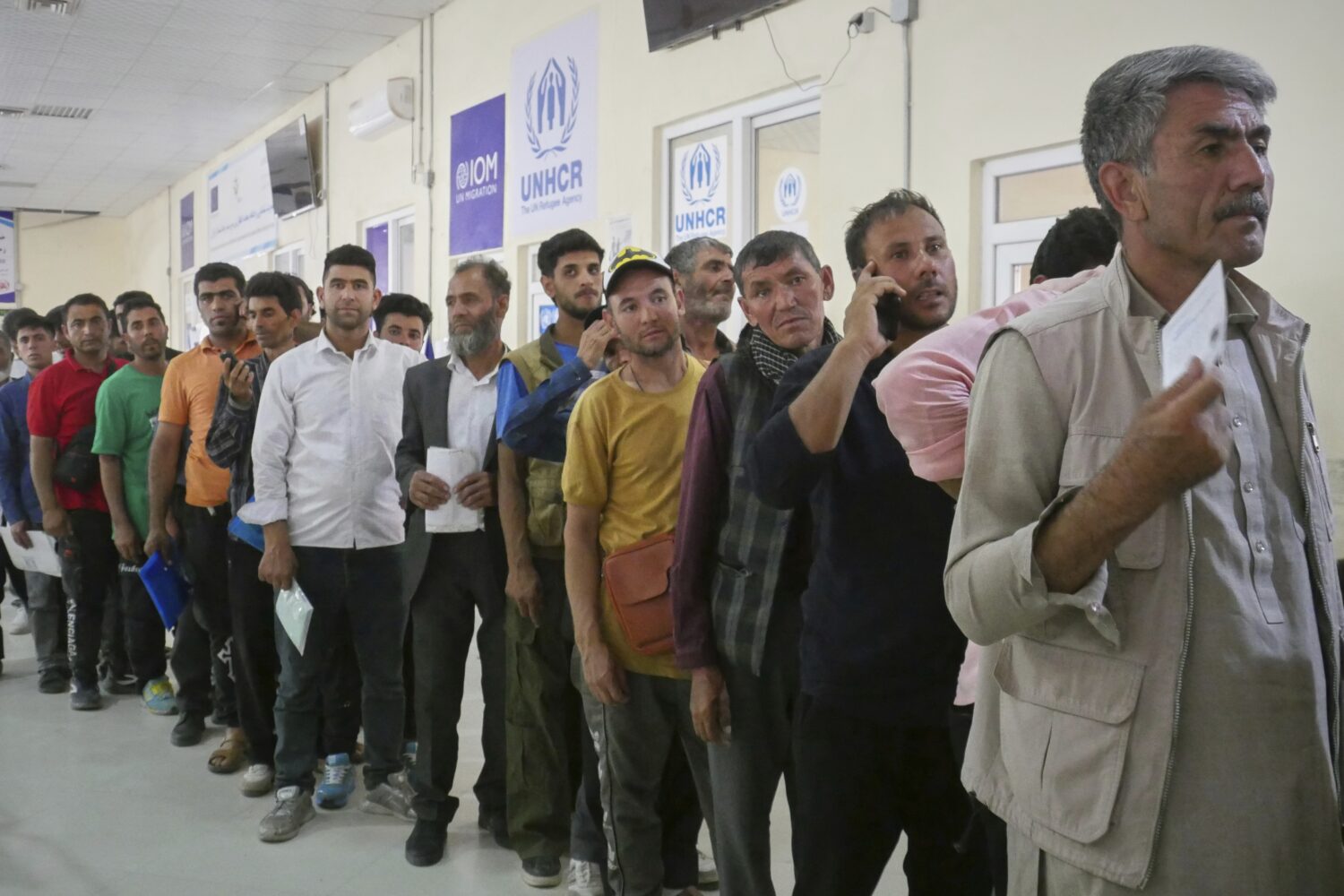 Afghan refugees who returned after fleeing Iran to escape deportation and conflict line up at a UNH...