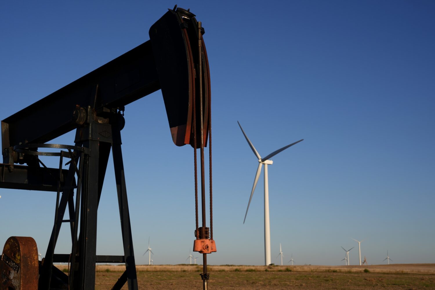 FILE - Pumpjacks operate in the foreground while a wind turbines at the Buckeye Wind Energy wind fa...