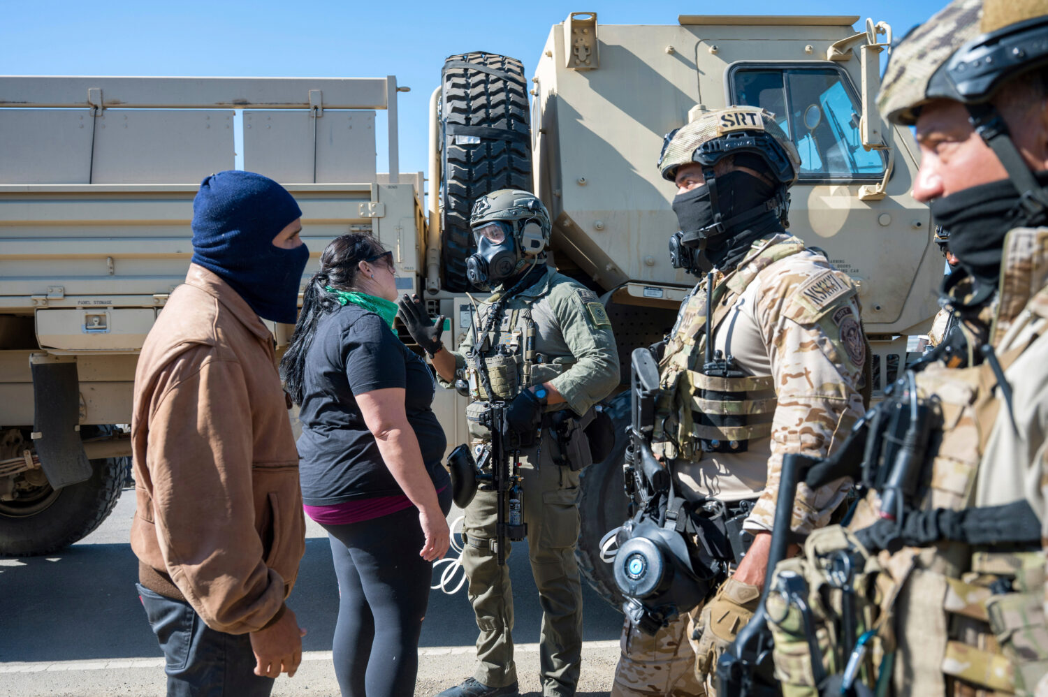 Federal immigration agents talk to Rebecca Torres, second left, after she tried to block a military...