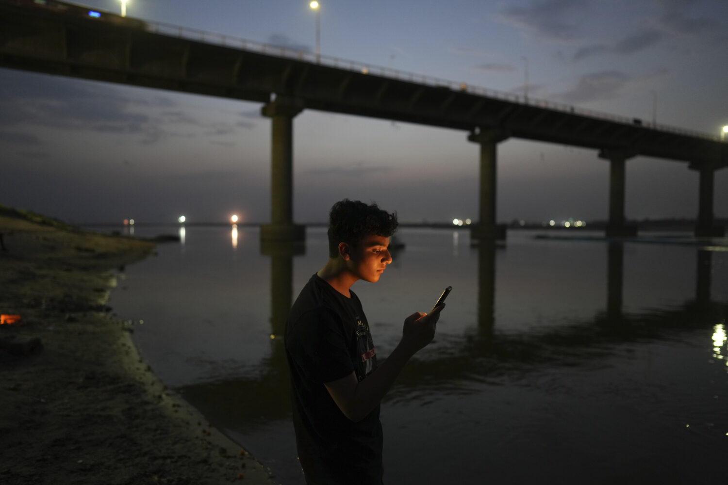 FILE - A youth checks his mobile phone on the bank of the River Ganges in Prayagraj, India, June 7,...