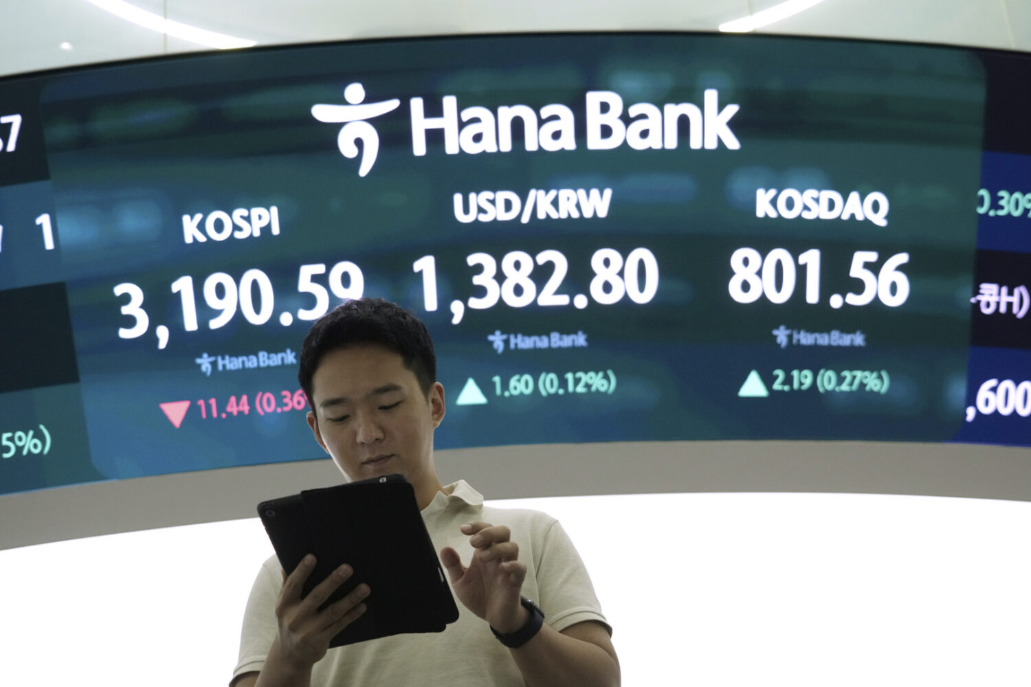 A currency trader works near a screen showing the Korea Composite Stock Price Index (KOSPI), top le...