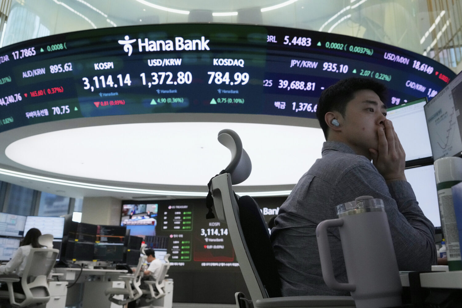 A currency trader watches monitors near a screen showing the Korea Composite Stock Price Index (KOS...