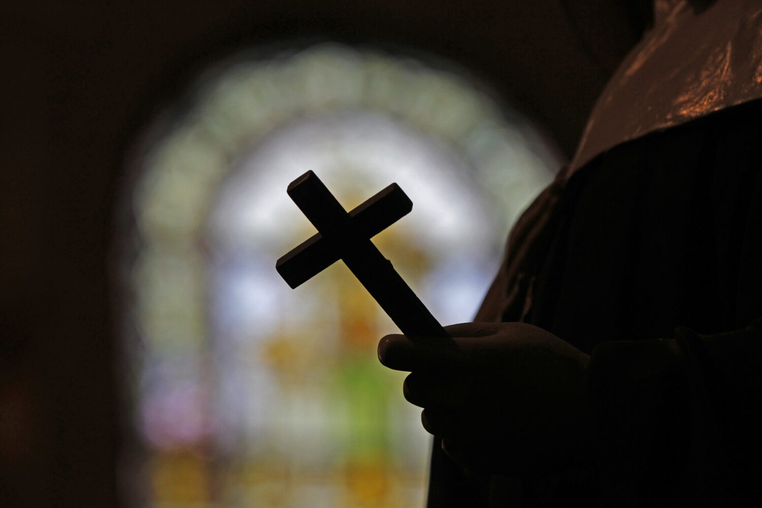 FILE - A crucifix is silhouetted against a stained glass window inside a Catholic Church in New Orl...