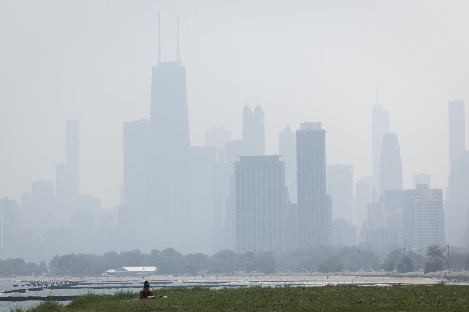 People sun tan in grass off the Lakefront Trail on the North Side as a haze of Canadian wildfire sm...