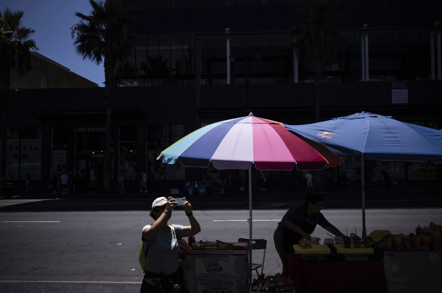 A visitor takes pictures of the TCL Chinese Theatre as a street vendor works nearby in the Hollywoo...