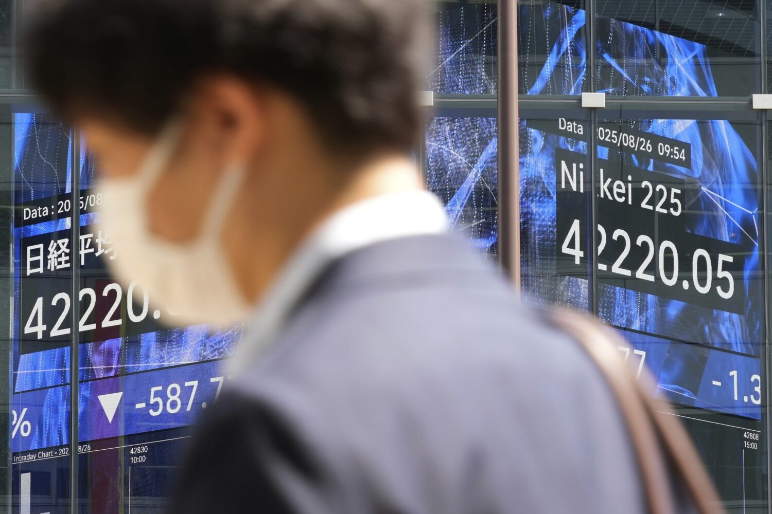 A person walks in front of an electronic stock board showing Japan's Nikkei index at a securities f...