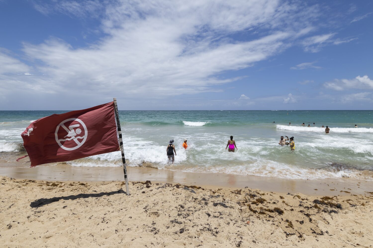 A warning flag flies on the beach as people swim in Condado, Puerto Rico, as Hurricane Erin approac...