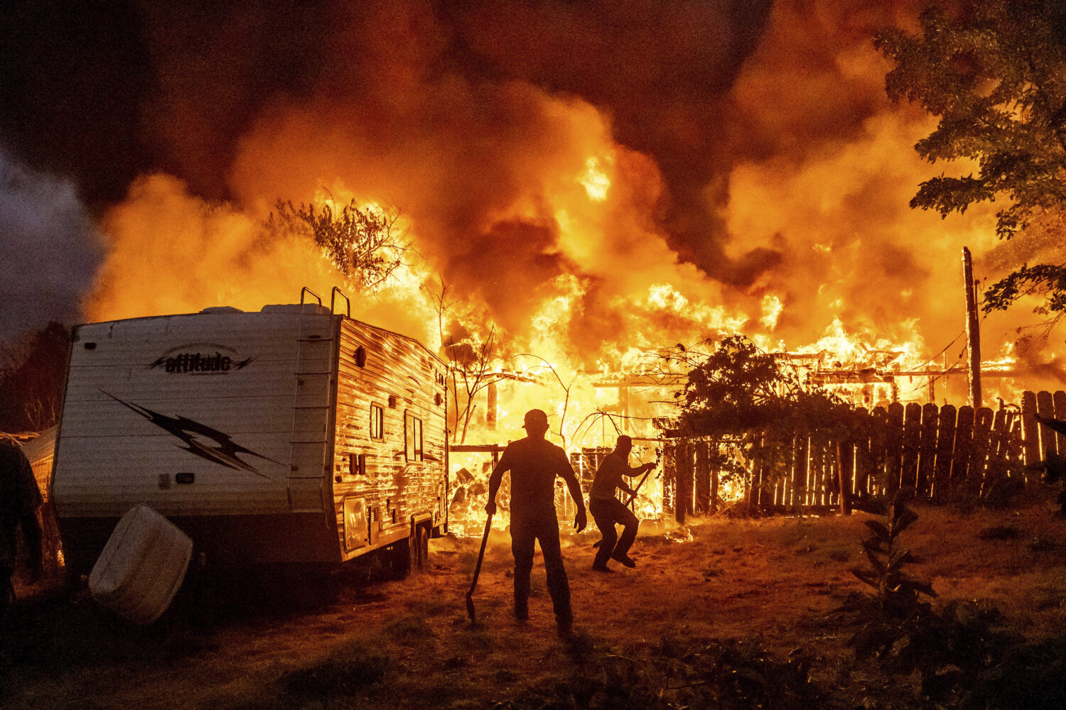 Residents work to stop flames from a burning home from spreading to a neighboring house as the 6-5 ...