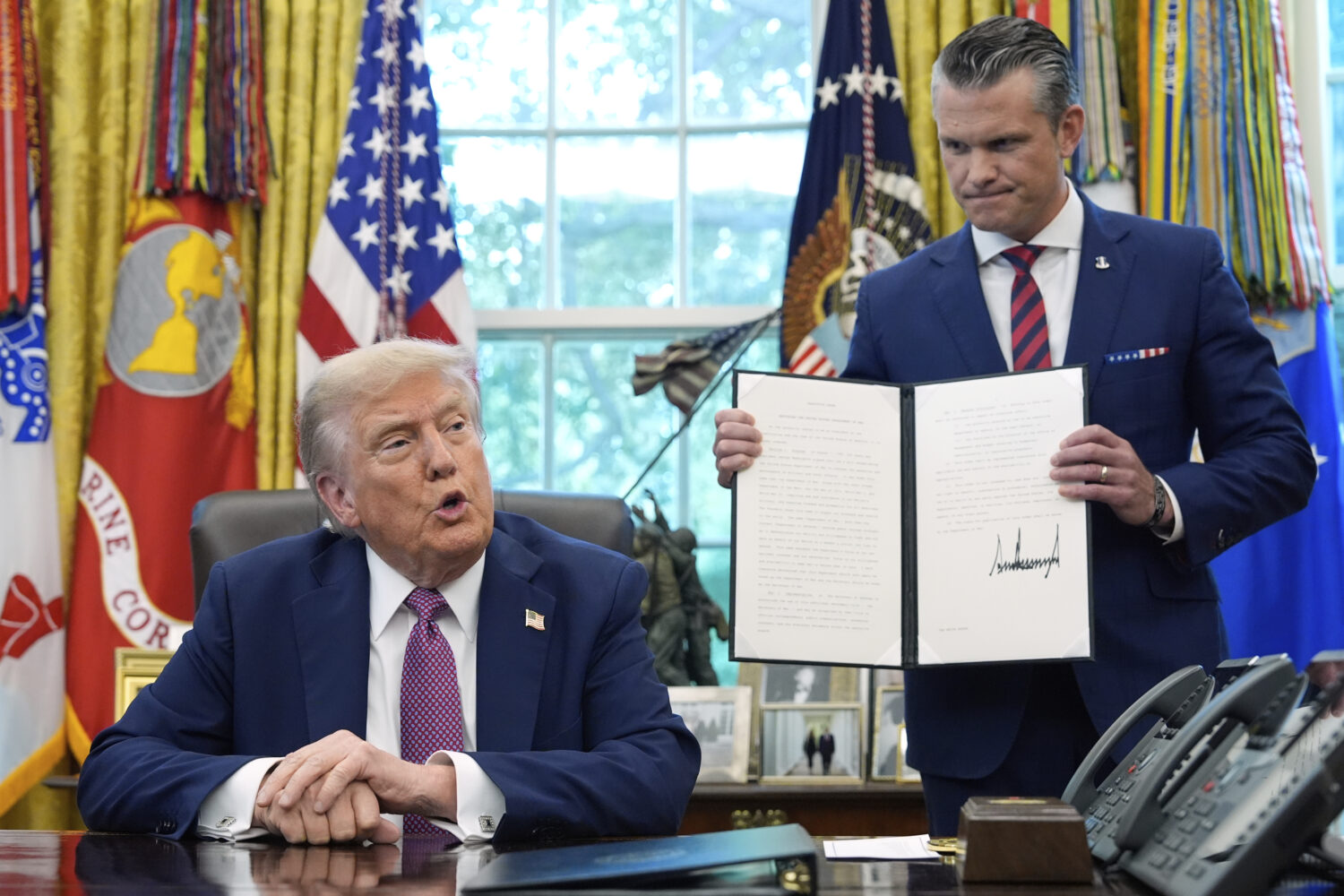 President Donald Trump speaks as Defense Secretary Pete Hegseth holds a signed executive order in t...