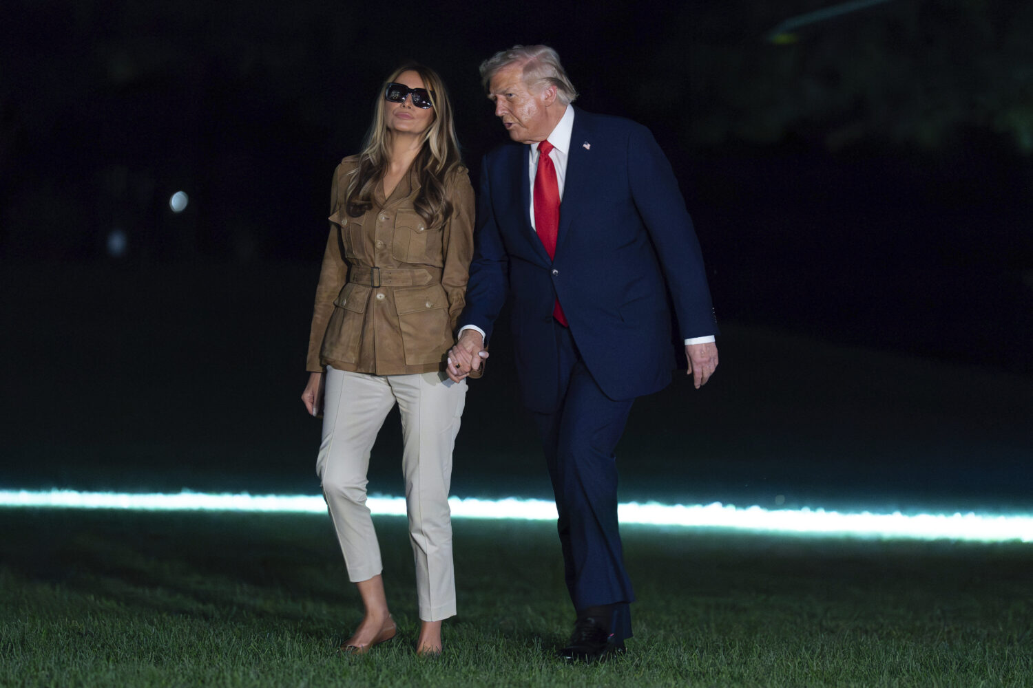 President Donald Trump holds hands with first lady Melania Trump as they walk on the South Lawn upo...