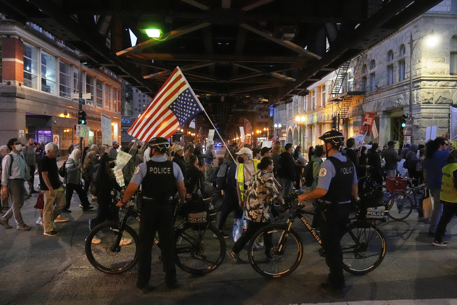 Police officers block a street as demonstrators march at a protest opposing "Operation Midway Blitz...