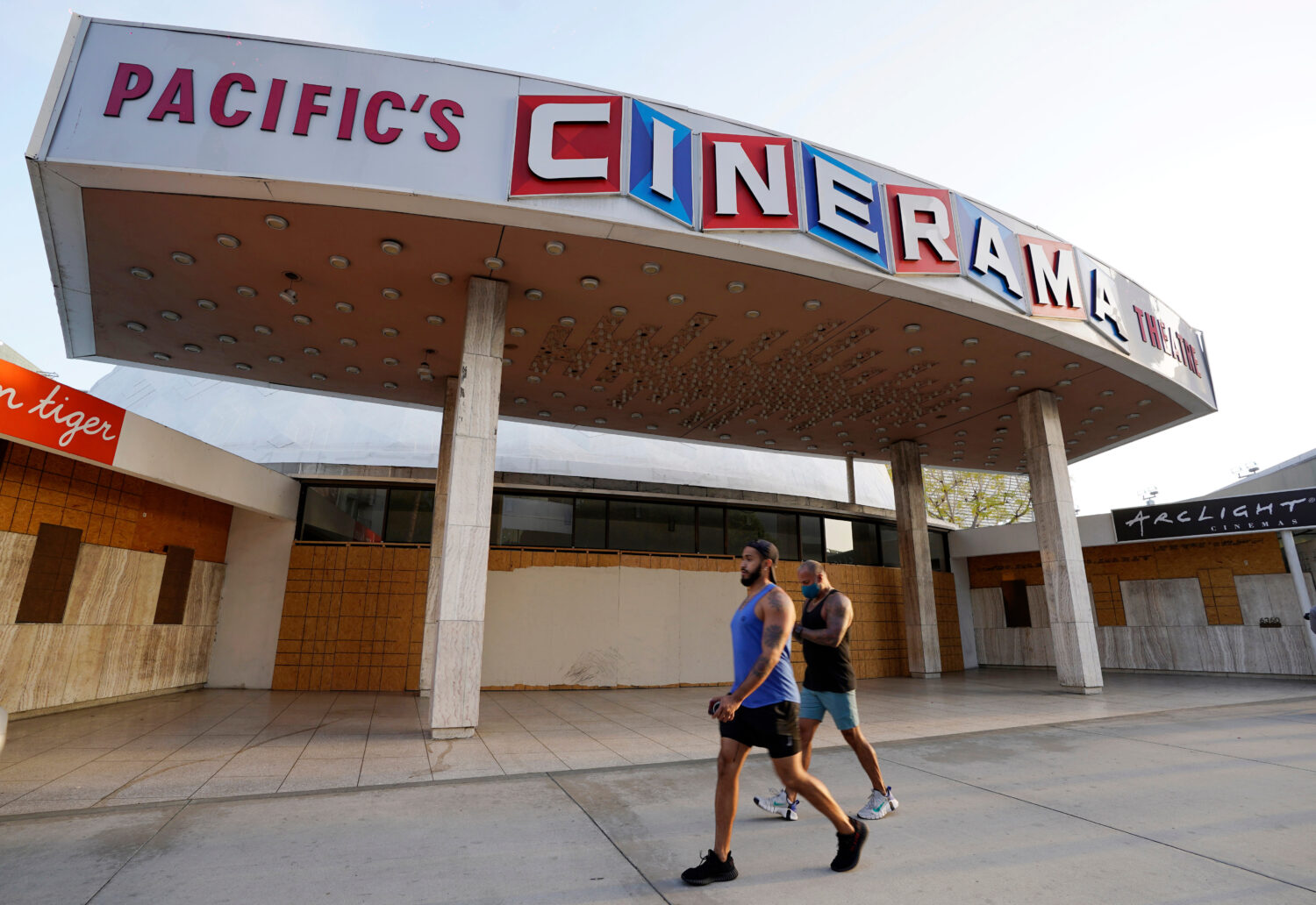 FILE - Pedestrians walk past the boarded up and closed Cinerama Dome movie theater, April 12, 2021,...