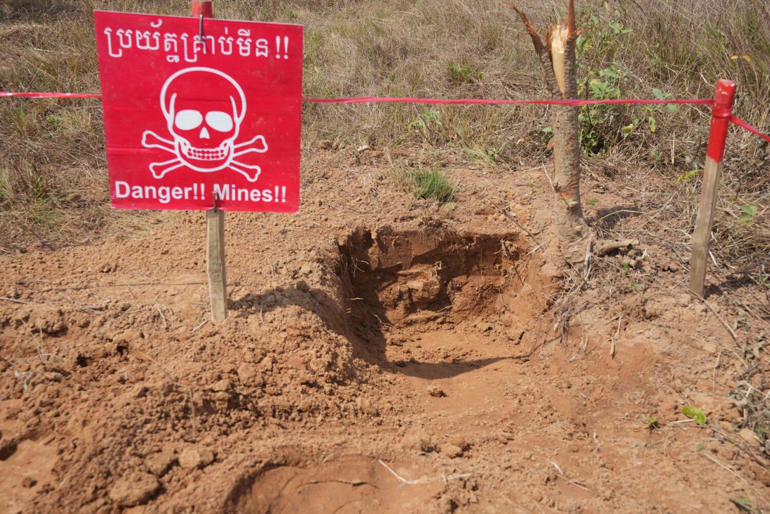 FILE - A "Danger Mines" sign marks an area as Cambodia Mine Action Center, CMAC, staff members work...