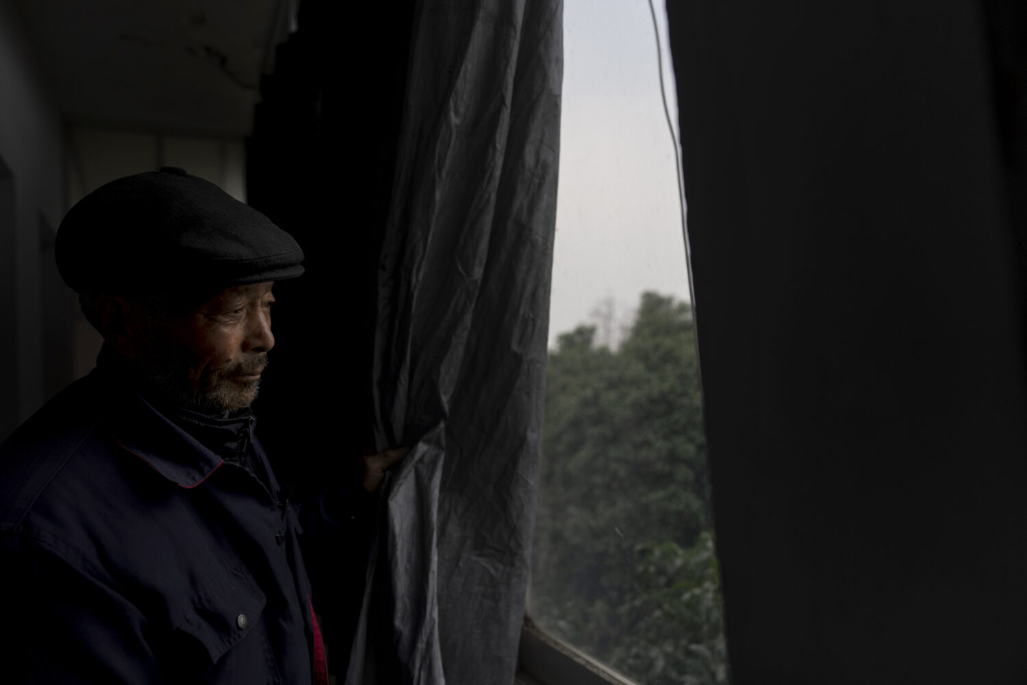 Petitioner Yang Guoliang pulls back the blackout curtain used to provide privacy from nearby police...