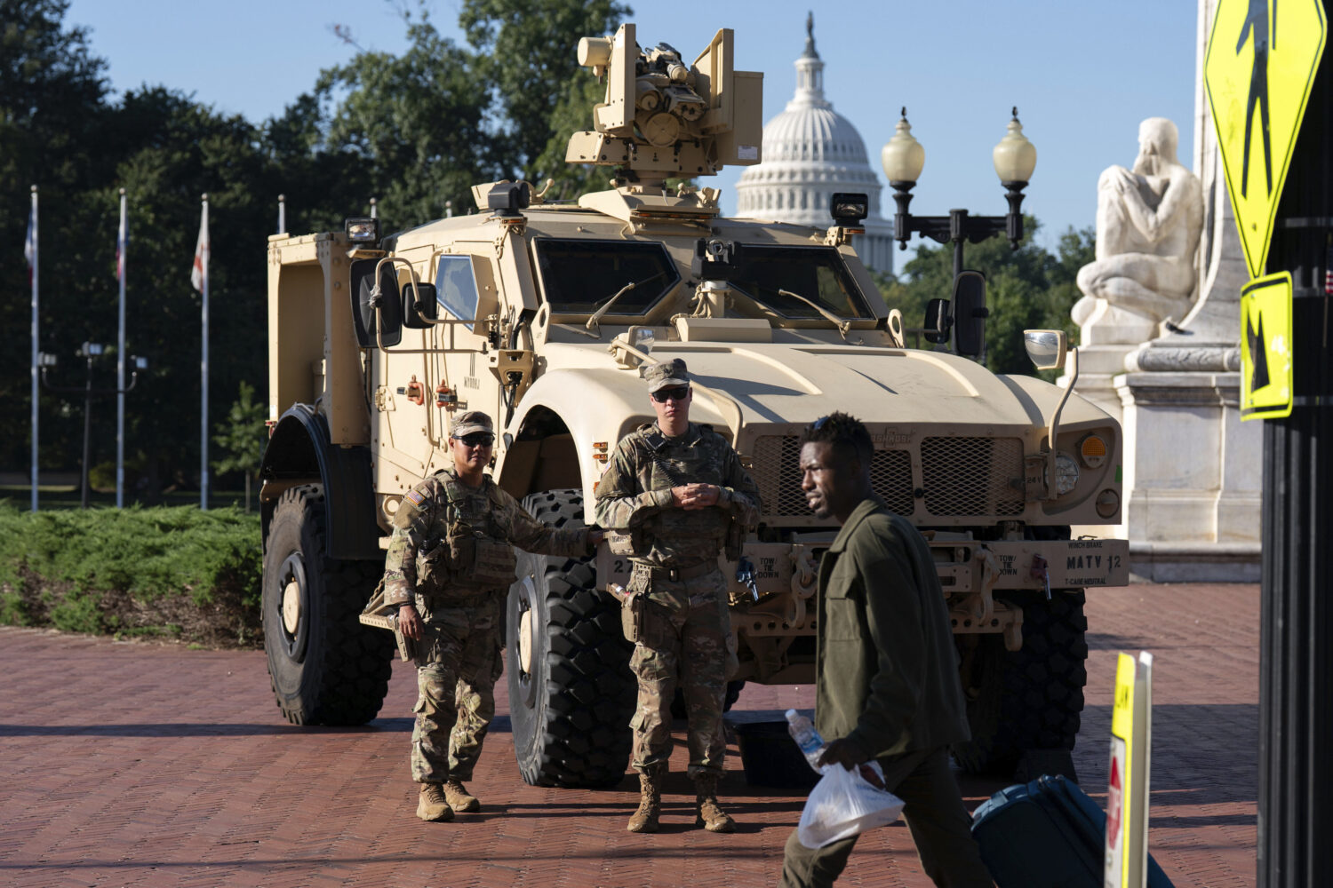 Members of the District of Columbia National Guard standing next to an MATV vehicle scan the area a...