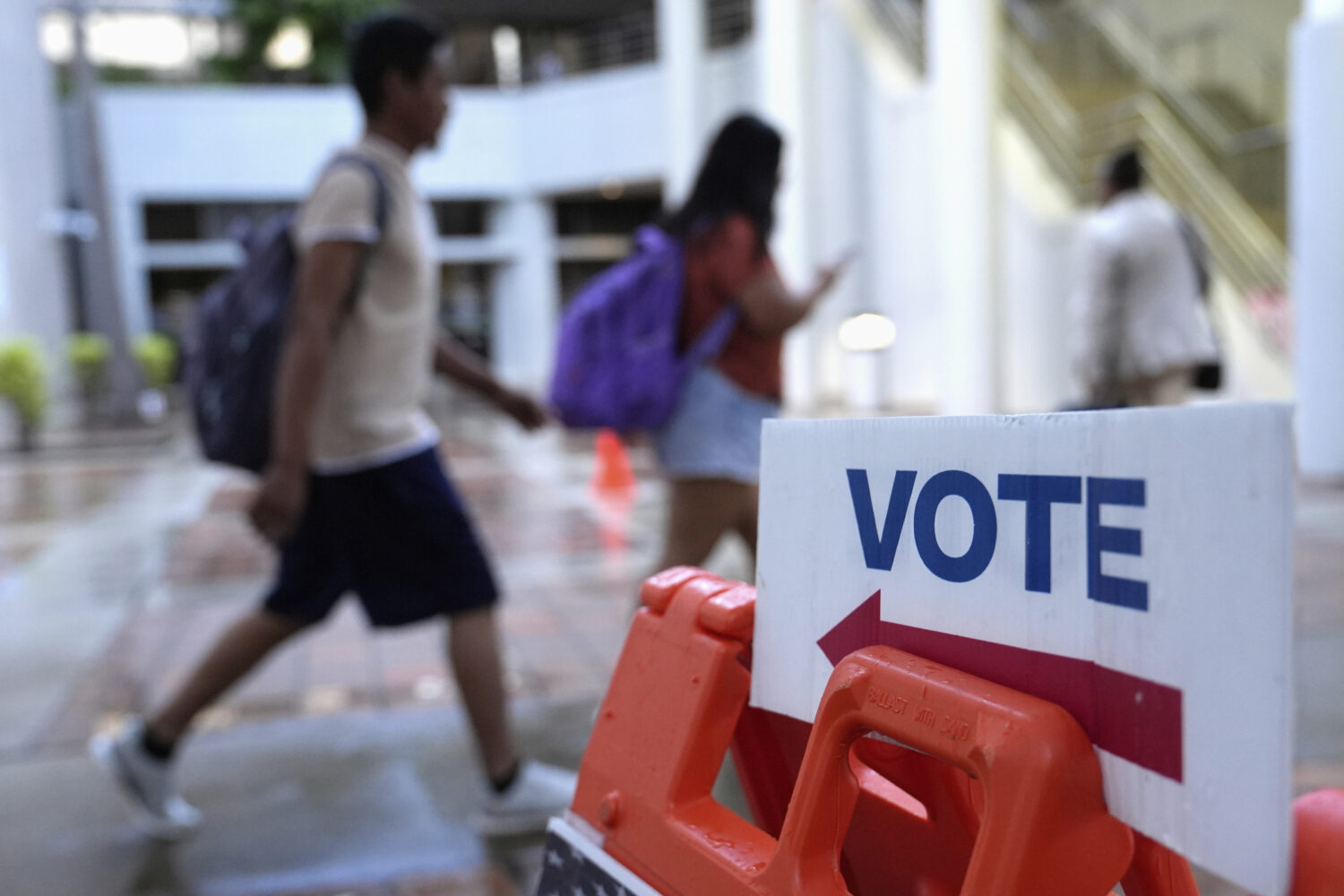 FILE - People walk past a "vote" sign on the first day of early voting in the general election in M...