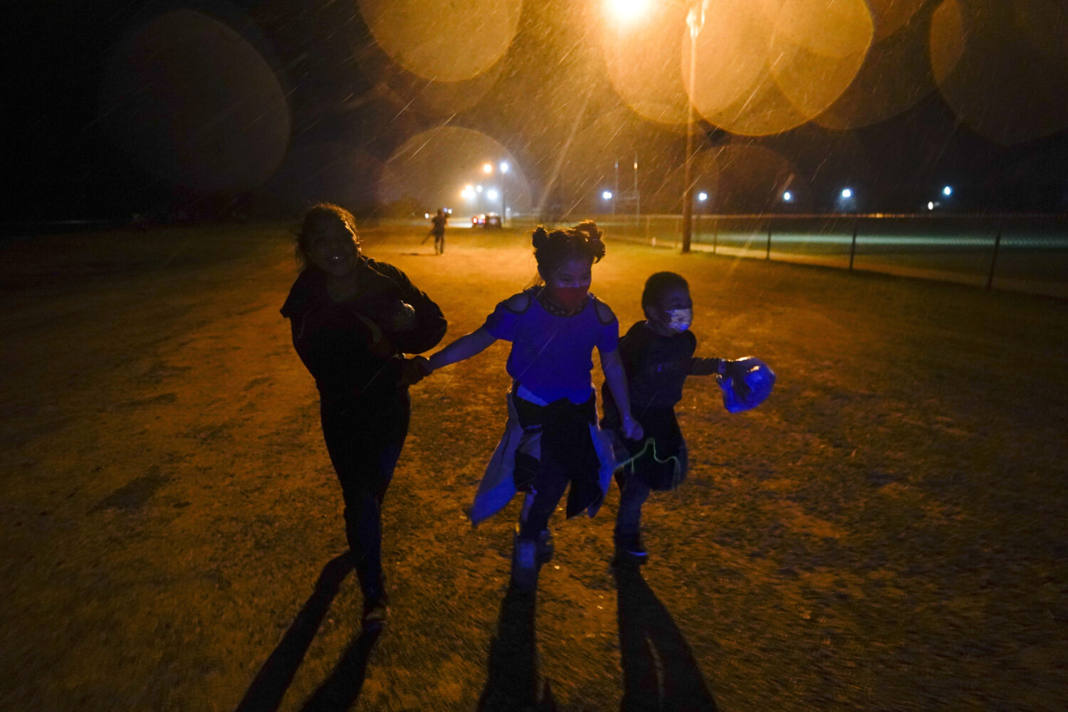 FILE - Young migrants hold hands as they run in the rain at an intake area after turning themselves...