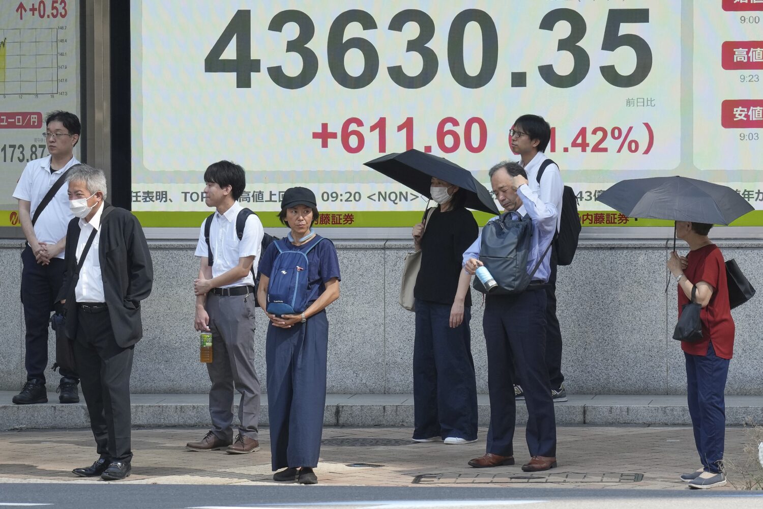 People stand in front of an electronic stock board showing Japan's Nikkei index at a securities fir...
