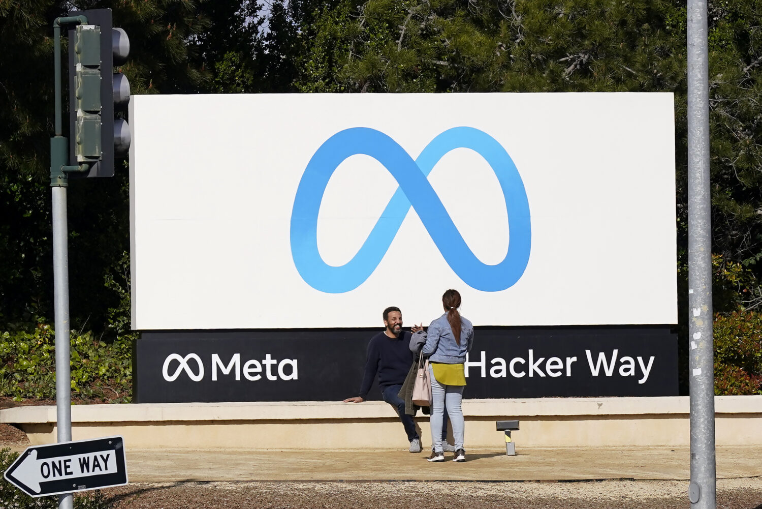 FILE - People talk near a Meta sign outside of the company's headquarters in Menlo Park, Calif., Ma...