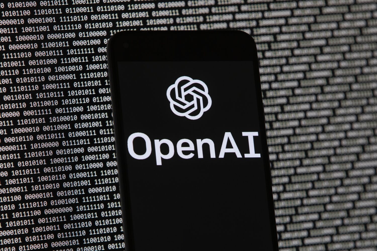 FILE - The OpenAI logo appears on a mobile phone in front of a computer screen with random binary d...