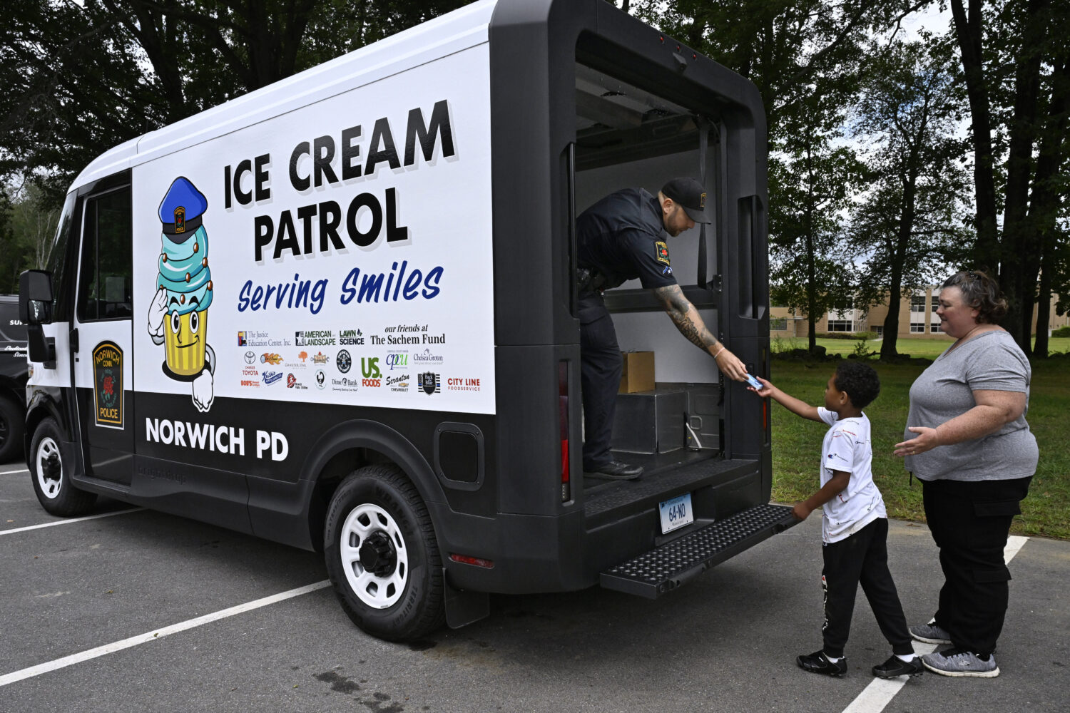 Norwich Police School Resource Officer Bob McKinney hands an ice cream to Alby Little as his mother...