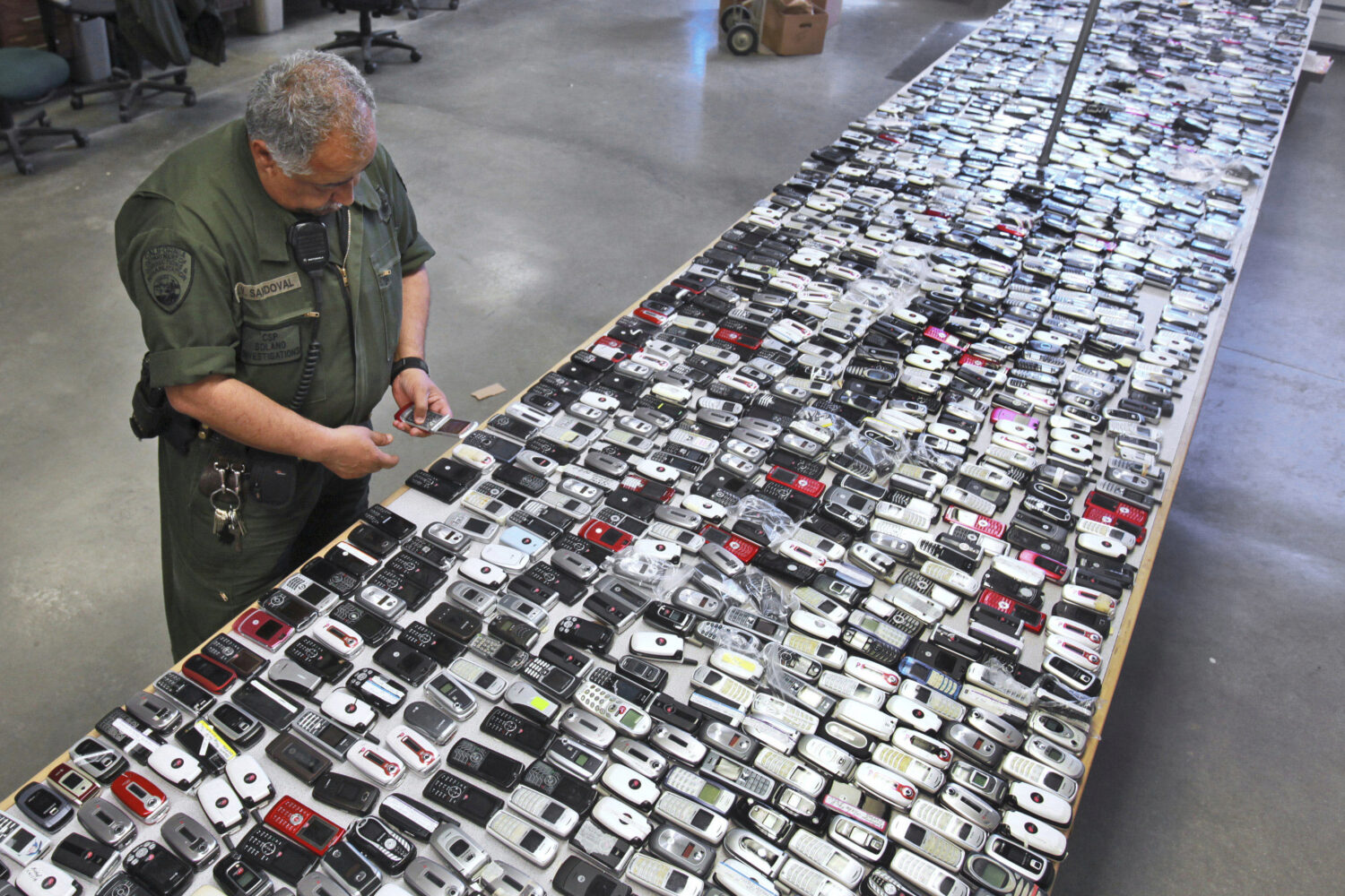 FILE - Correctional Officer Jose Sandoval inspects one of the more than 2,000 cell phones confiscat...