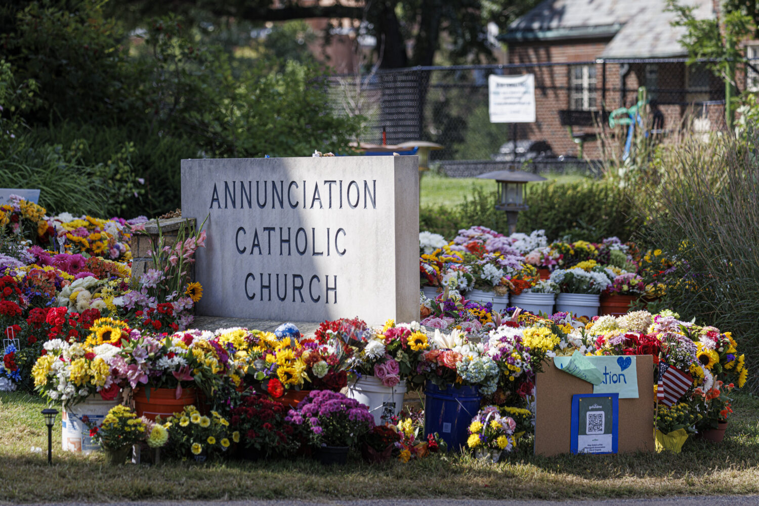 A vibrant memorial of flowers and tributes surrounds a sign for Annunciation Catholic Church in Min...