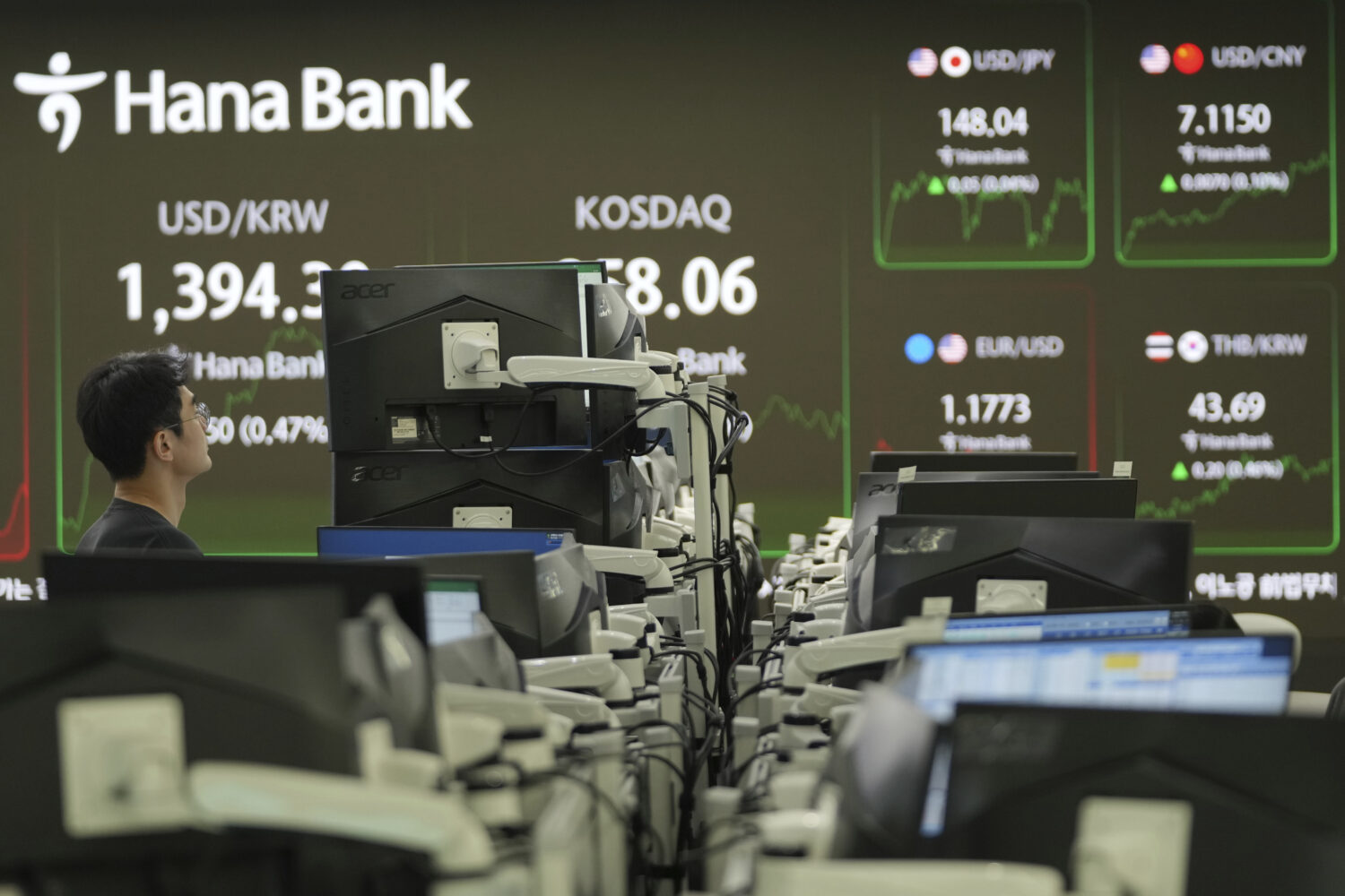 A dealer watches computer monitors near the screens showing the foreign exchange rates at a dealing...