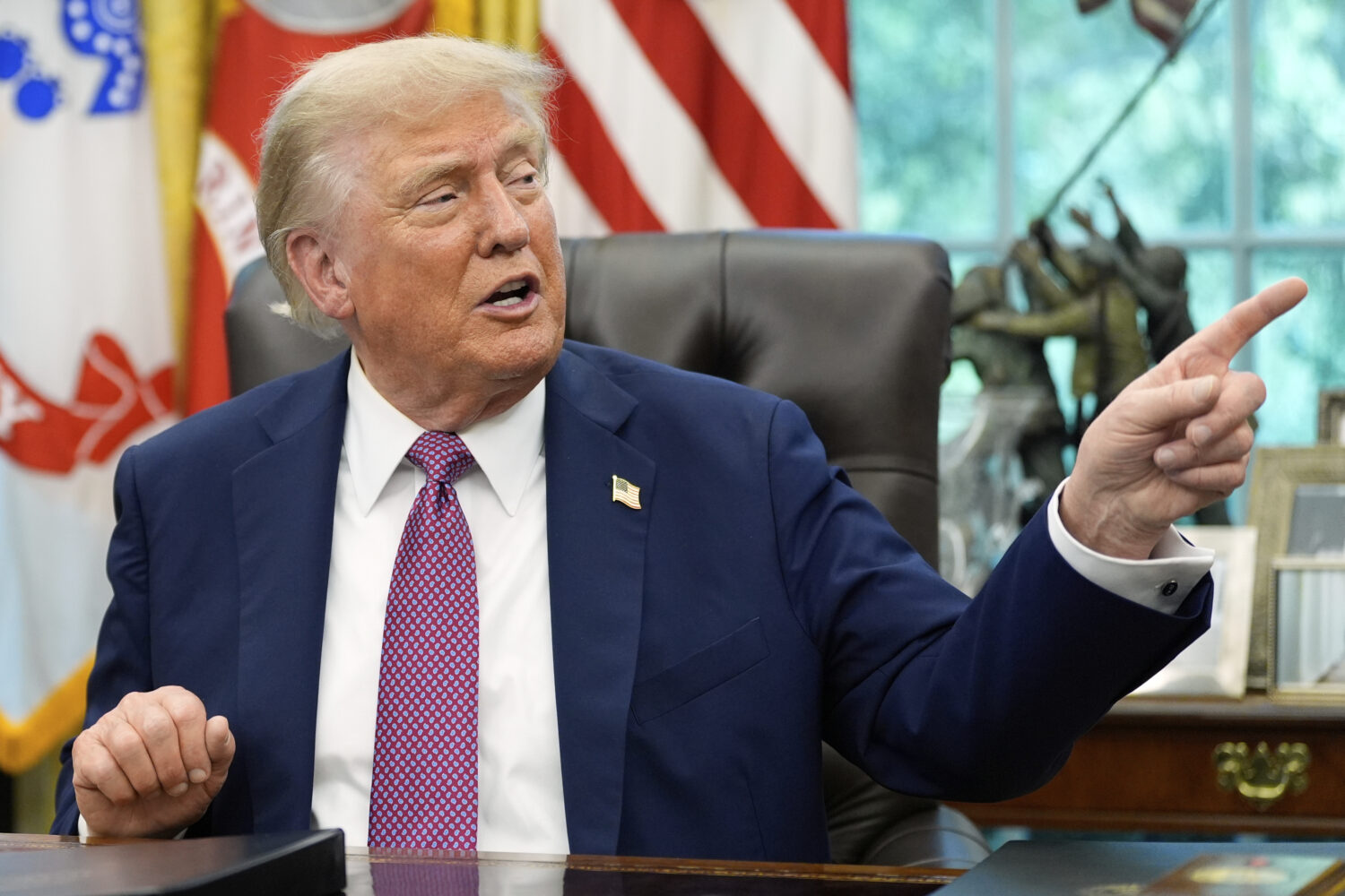 President Donald Trump point to a G20 Miami 2026 poster as he speaks in the Oval Office of the Whit...