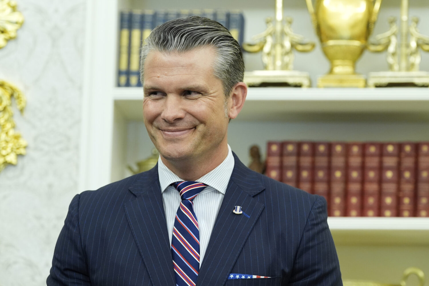 Defense Secretary Pete Hegseth listens as President Donald Trump speaks during an event signing a p...