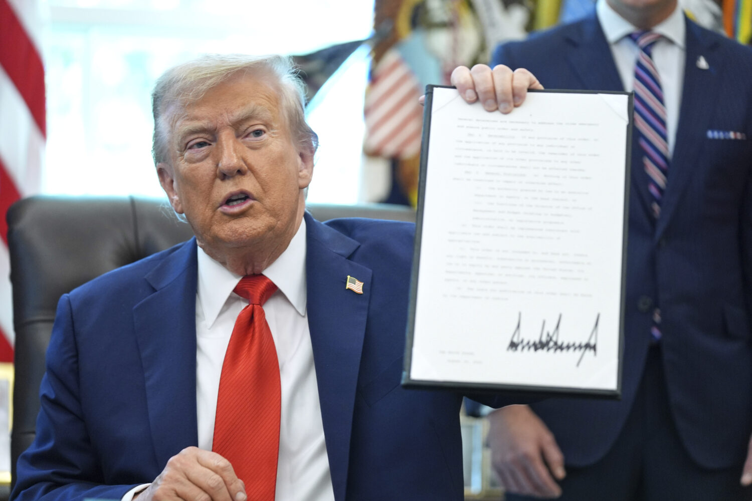 President Donald Trump holds up a signed executive order requiring the Justice Department to invest...